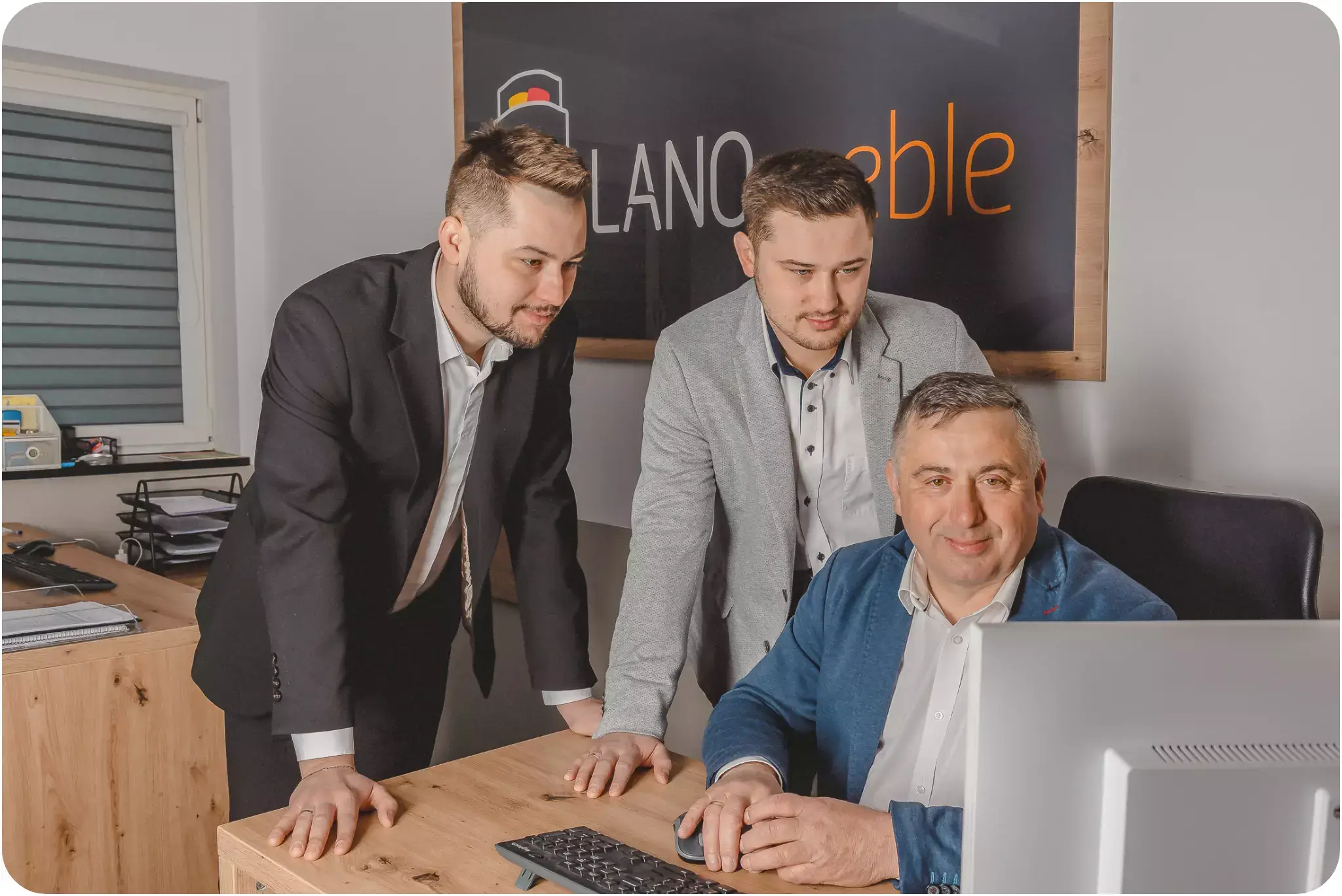 Photo of the founders of the LANO brand, father sitting at the desk, two sons standing behind him